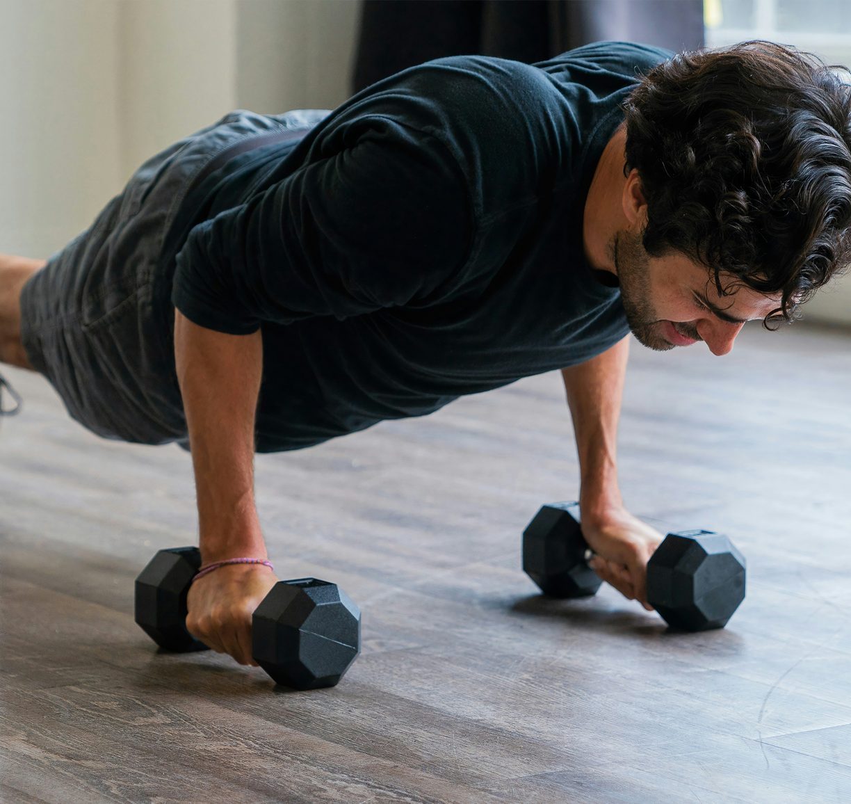 Un hombre hace flexiones apoyado en dos mancuernas.